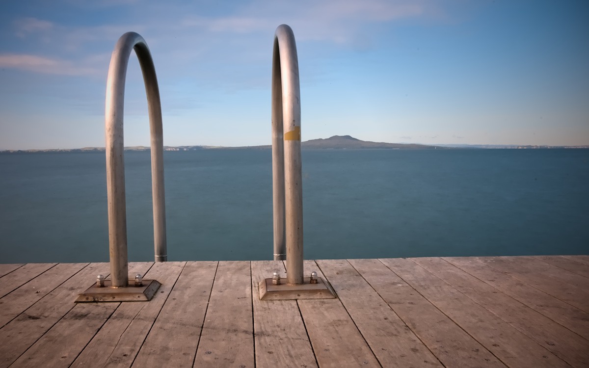 Rangitoto Island in the distance over the sea with a jetty swim ladder in the foreground