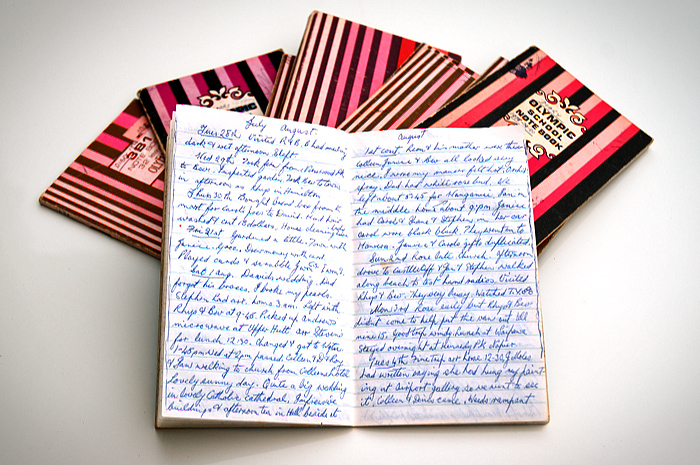 A small pile of 3b1 notebooks, one open showing illegible writing